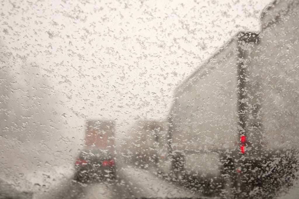 Cars and trucks driving on snow packed roads taken through a windshield covered with snowflakes.