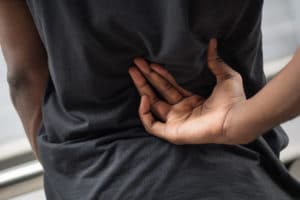 man suffering from back pain; sick african man with back joint pain, osteoporosis, bone arthritis, gout, symptoms; body sickness, health care or pain concept; adult african man or black man model